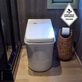Load image into Gallery viewer, Cinderella Comfort incineration toilet in a bathroom with a woven basket and toilet paper roll.