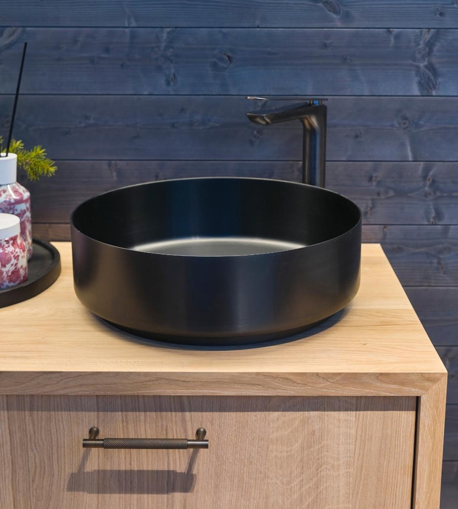 Black oval sink on a wooden cabinet with a wooden wall background
