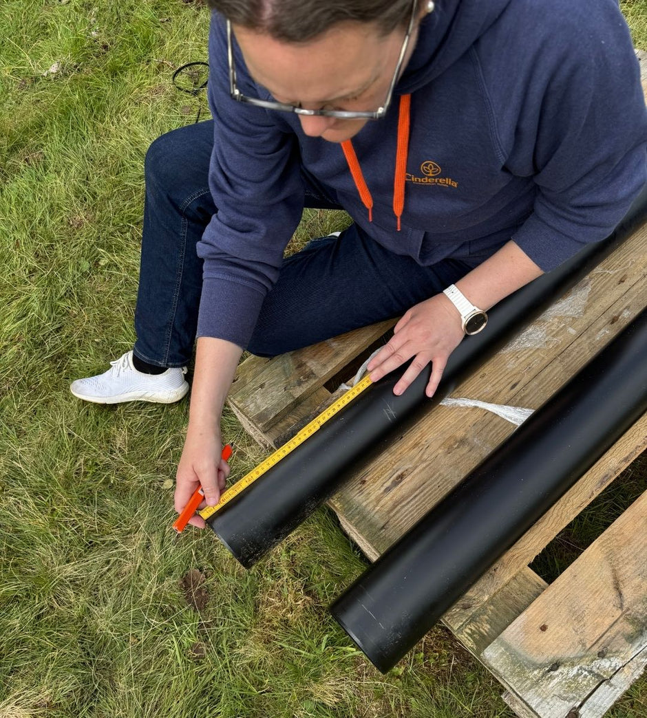 Eine Person misst ein schwarzes Rohr auf einer Holzpalette im Freien