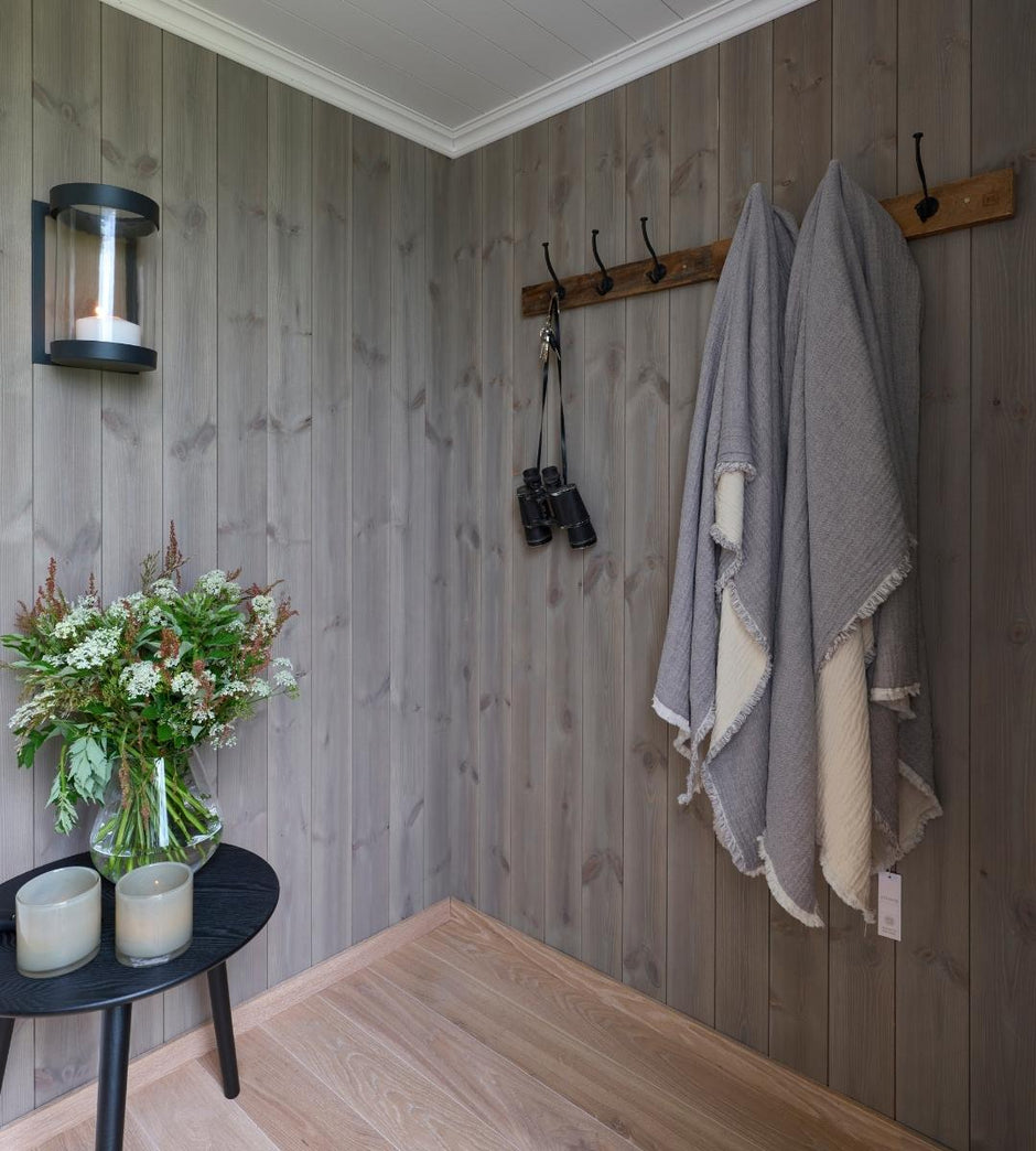 Pared de madera con ganchos, un jarrón con flores y velas sobre una mesita.