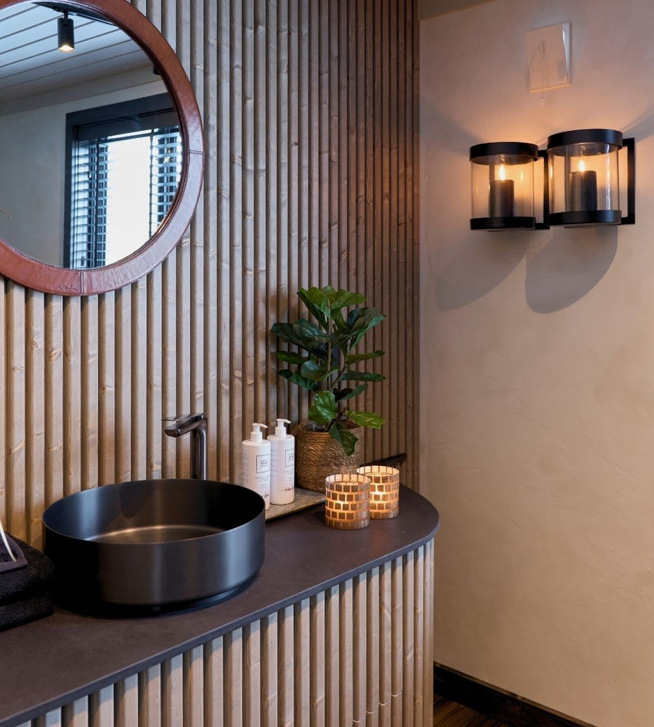 Cuarto de baño con espejo redondo, lavabo negro y elementos decorativos.