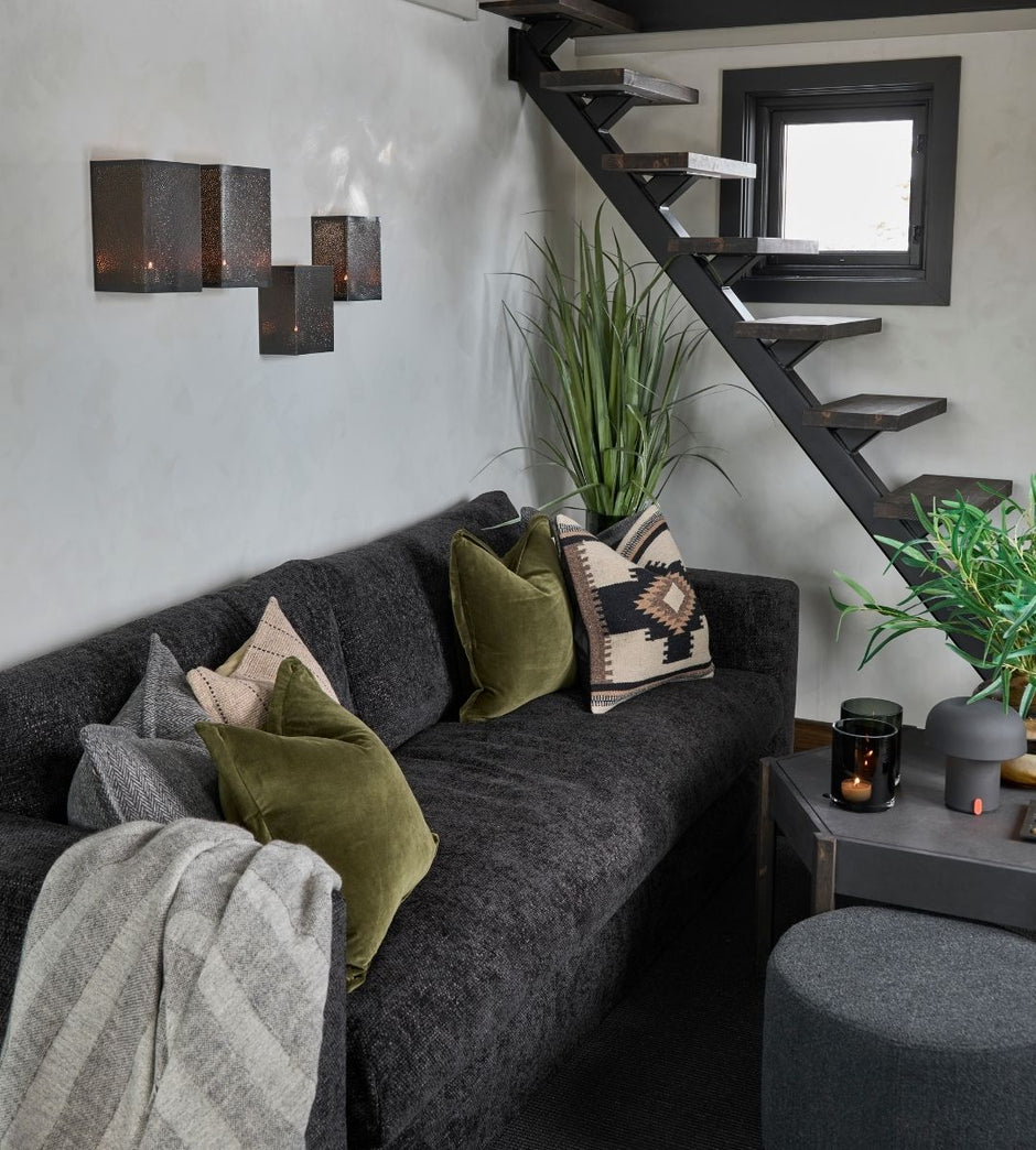 Salón con un sofá seccional gris, cojines decorativos y una escalera al fondo.