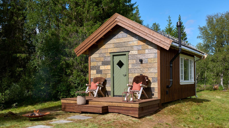 Pequeño anexo de madera en un entorno forestal con terraza y muebles de exterior.