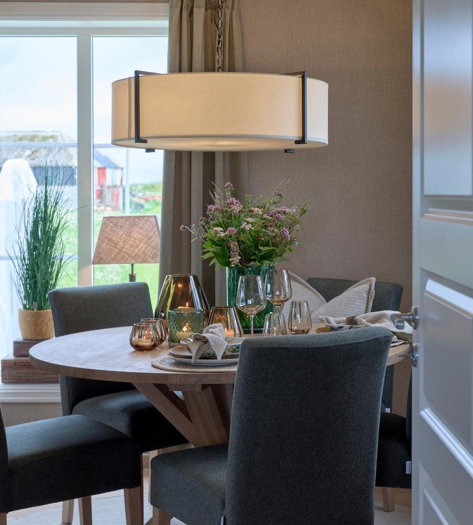 Salle à manger avec une table ronde dressée pour un repas, avec des chaises, une lampe et des éléments décoratifs.