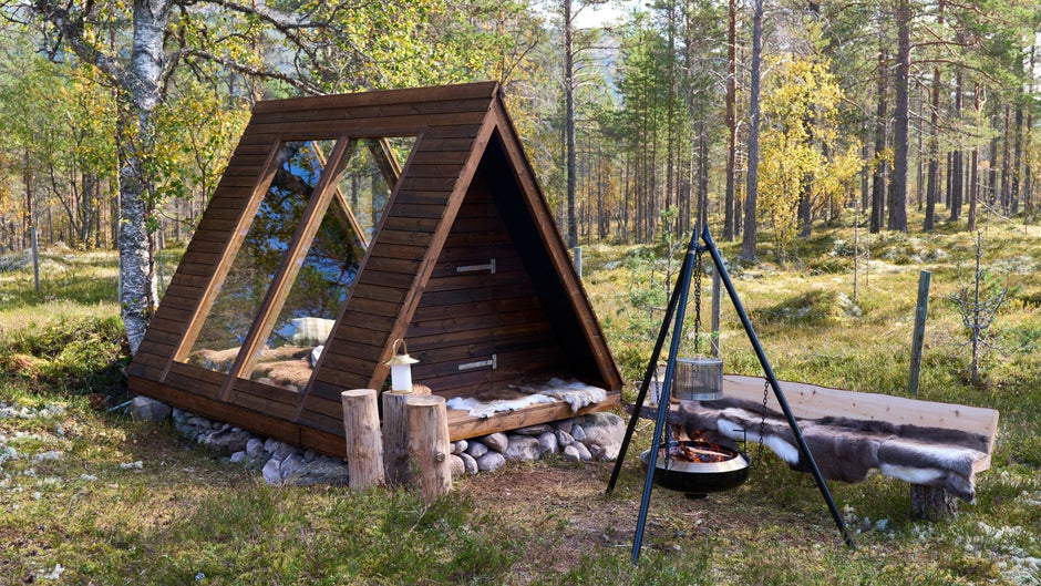 Trehytte i en skog med bålplass og sittegruppe.