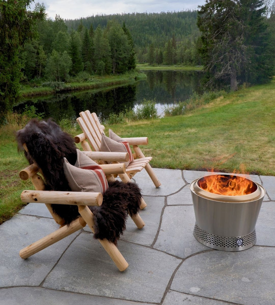 To trestoler ved et bål med naturskjønn utsikt over en innsjø og skog.